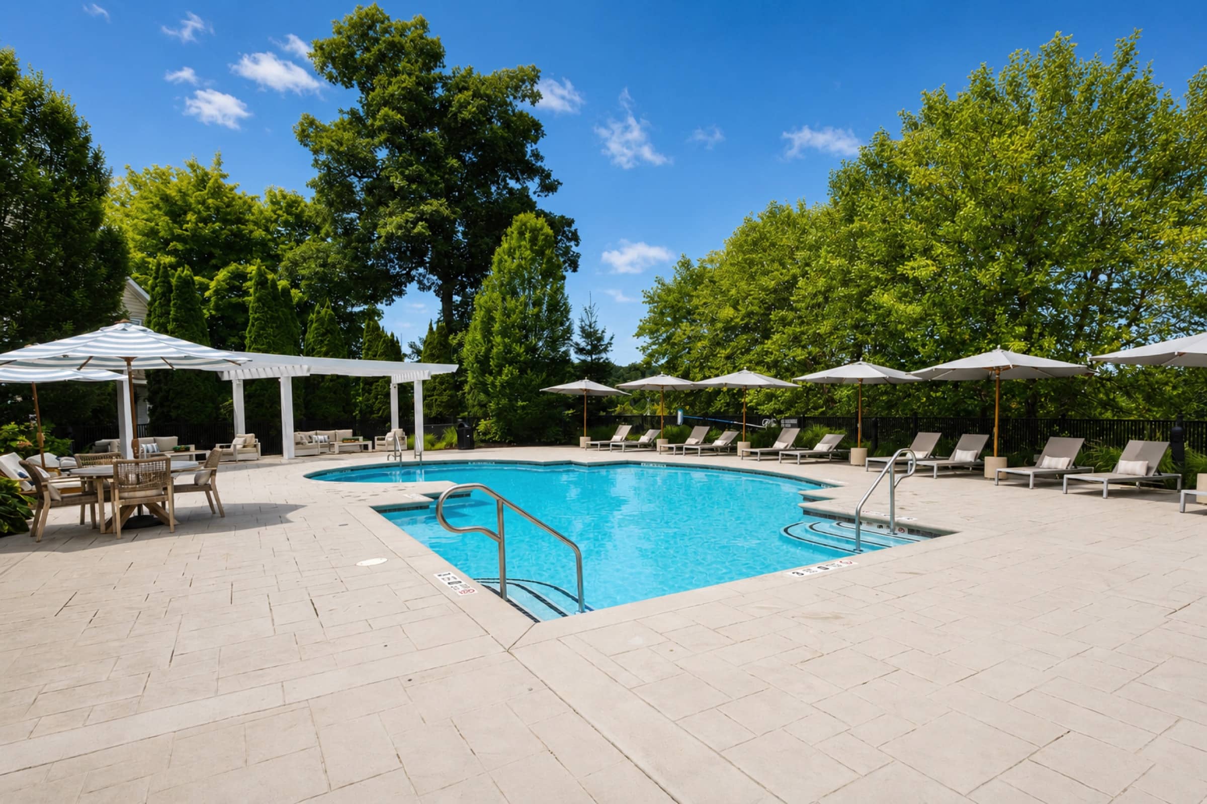 Pool deck at White Oaks with striped umbrellas, pergola lounge, and rows of sun loungers