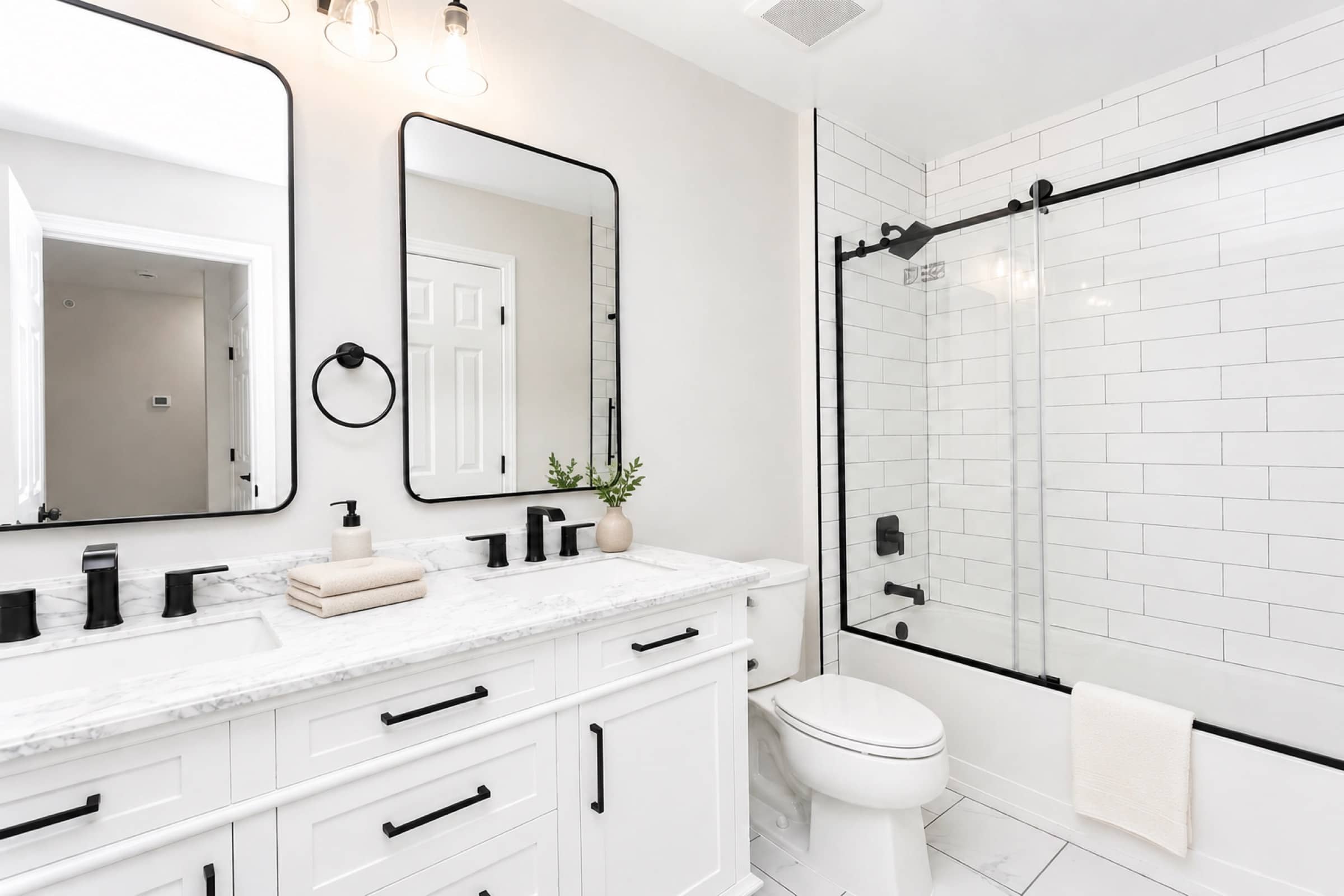 Renovated double-vanity bath with marble top and glass shower at White Oaks (virtually staged)